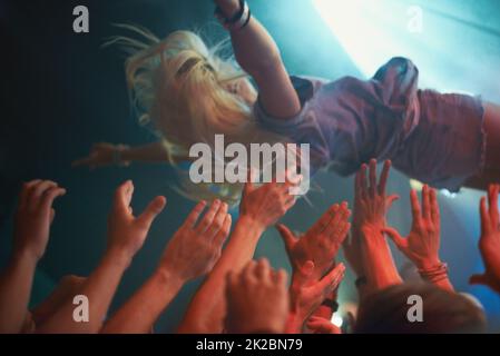 Surfing on a wave of fans. A young woman crowd-surfing at a concert. Stock Photo