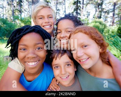 Fun, friends and fresh air. A closeup of image of a group of kids smiling at the camera while standing in the woods. Stock Photo