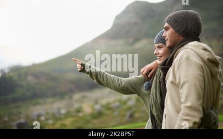 This view is stunning. A young couple admiring the view while out hiking during winter. Stock Photo