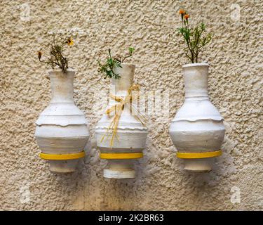 Three adjacent handmade white pottery vases, hanged on rough stone white wall Stock Photo