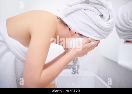 Final stages of her beauty treatment. A young woman washing off her facial mask in her bathroom. Stock Photo