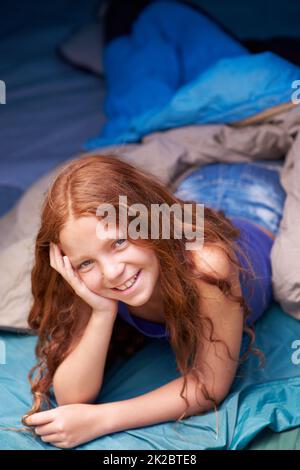 She loves camping. Portrait of a happy young girl lying in her tent while camping. Stock Photo