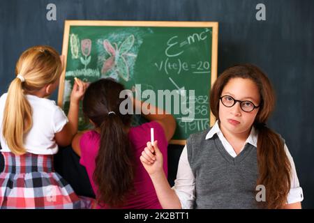 She prefers to study than play. Portrait of a cute brunette girl with two classmates playing on the chalkboard in class. Stock Photo