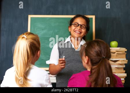 Shes happy to help her friends. Portrait of a cute girl teaching her two classmates something using the chalkboard i class. Stock Photo