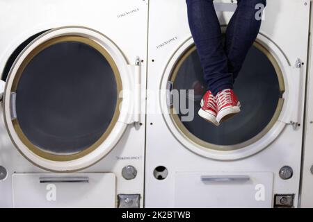 Relaxed at the laundromat. Cropped image a mans legs as he sits on a washing machine at the laundromat. Stock Photo