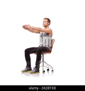 Keeping his limbs long and lean. A handsome young man wearing gym clothes and stretching while seated in an office chair against a white background. Stock Photo