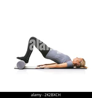 Arching her back. A young woman lying on an exercise mat and using a foam roller to arch her back. Stock Photo