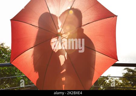 Hidden love. Silhouette of an affectionate couple standing behind an umbrella. Stock Photo