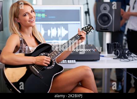 This song is going to be a hit. A gorgeous blonde guitarist sitting in a recording studio with her instrument. Stock Photo