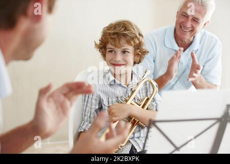 Supporting his talent. Shot of a cute little boy looking pleased as his father and grandfather cheer him on after playing the trumpet. Stock Photo