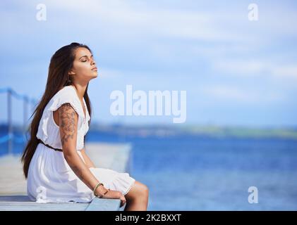 Quiet contemplations beside the sea. Cropped shot of a gorgeous tattooed young woman sitting on a pier. Stock Photo