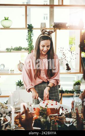 Guys Im cutting the cake. Cropped shot of an attractive young woman cutting the cake during Christmas lunch with her friends at home. Stock Photo