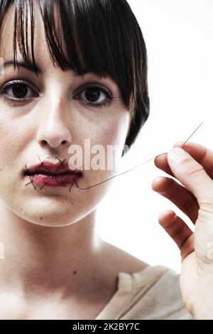 She can no longer speak up. A young woman having her mouth sewn shut. Stock Photo