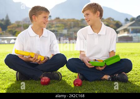 What do you have for lunch. Two young schoolboys sitting on the grass about to eat their lunch. Stock Photo