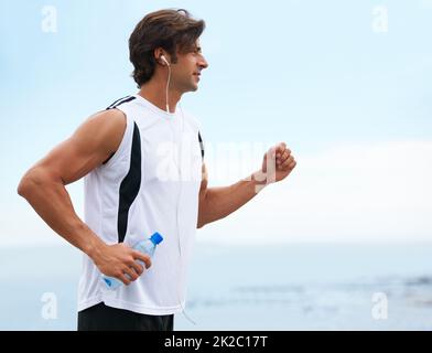 Nothing can hold him back. Profile view of a handsome man holding a water bottle, going for a run and listening to music - copyspace. Stock Photo