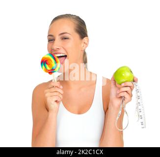 I thought Id reward myself.... Portrait of a sporty young woman licking a lollipop while holding an apple. Stock Photo