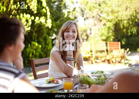 Chatting over a healthy meal. Smiling young woman at a lunch with a group of friends. Stock Photo