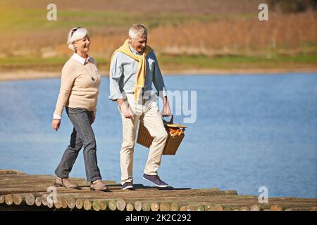 Taking a walk on the carefree side of life. Shot of a happy senior couple walking along the pier of a lake. Stock Photo