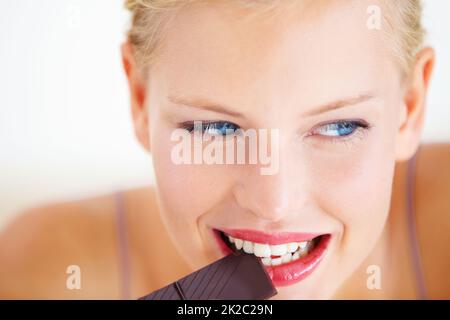 Nibbling on a decadent treat. Smiling young woman enjoying a delicious piece of chocolate. Stock Photo
