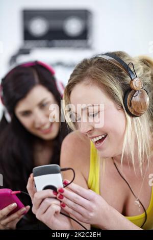 Enjoying the beat. Two young female friends listening to music on a mp3 player together. Stock Photo