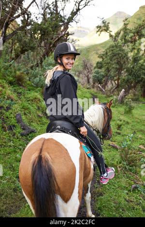 Horse riding in the outback. An attractive young woman riding a horse on a mountain trail. Stock Photo