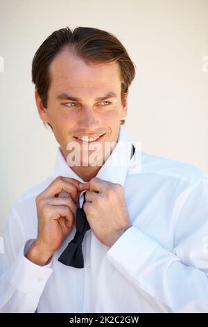 Getting ready for his big day. A handsome young man tying his bow tie. Stock Photo