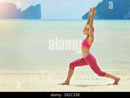 Working out to the sound of the waves. Shot of a focussed young woman doing yoga on the beach. Stock Photo