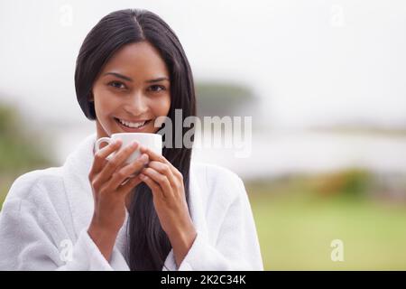 Enjoying her morning cup of coffee. A beautiful young woman enjoying a cup of coffee while wearing a bathrobe. Stock Photo