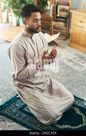 Prayer is devotion. Shot of a young muslim man praying in the lounge at home. Stock Photo