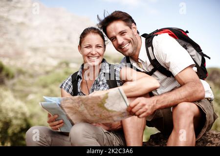 Taking the beaten track. Two hikers consulting their map while sitting on a mountain top. Stock Photo