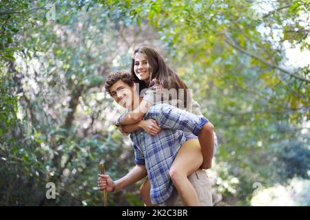 Young love in the woods. Portrait of a happy young man carrying his girlfriend on his back. Stock Photo