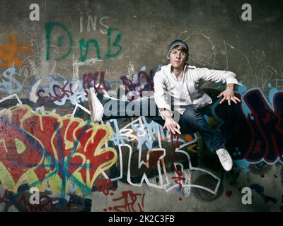 When the beat breaks free. Shot of a teenager breakdancer jumping against a spray painted wall. Stock Photo