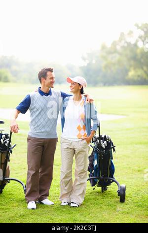Happy couple on golf course. Full length of happy golfing couple with arms around smiling and looking at each other. Stock Photo