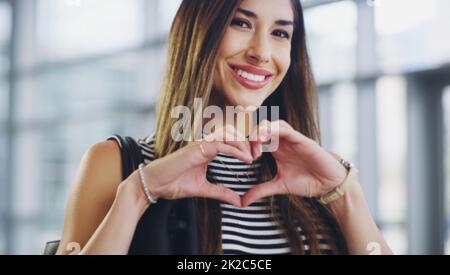 Ive poured my heart into being successful. Cropped shot of a young businesswoman showing a heart sign while walking through a modern office. Stock Photo