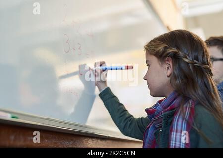 Shes got a bright young mind. Shot of an elementary school girl writing on a whiteboard in class. Stock Photo