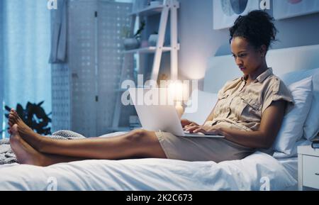 Time for some late night blogging. Shot of an attractive young woman using her laptop while lying on her bed after a long day at work. Stock Photo