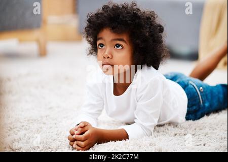 I dont like to be disturbed when I watch cartoons. Cropped shot of an adorable little boy lying down on a carpet and watching tv at home. Stock Photo