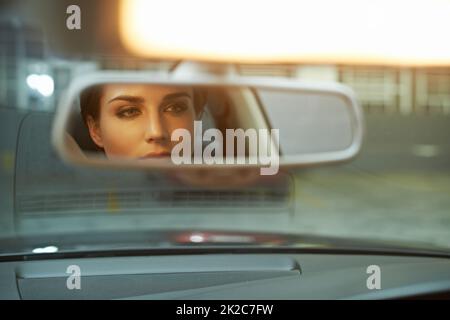 Checking her stylish appearance. A stylish woman checking her face in the rear view mirror. Stock Photo