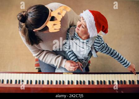 What awesome Christmas memories are made of. Shot of an adorable little boy playing the piano with his mother at Christmas. Stock Photo