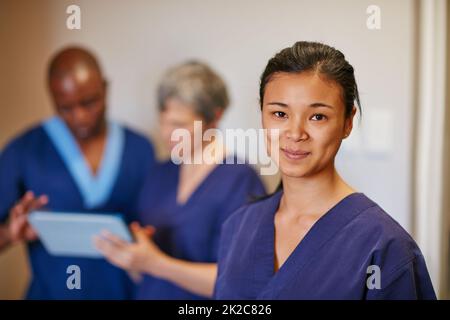 Helping people is so fulfilling. Cropped portrait of a female nurse standing in a hospital with her colleagues in the background. Stock Photo