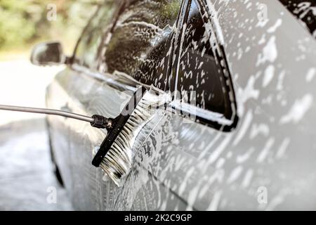 Side of silver car washed in self service carwash, brush leaving strokes in shampoo and foam. Stock Photo