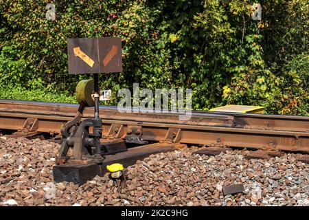 Old railway cross switch covered with black oil and dirt. Rail tracks and green bushes in background. Stock Photo
