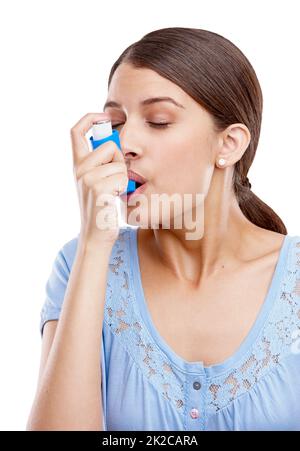 Luckily she had her inhaler with her. Studio shot of an attractive young woman using an asthma inhaler. Stock Photo