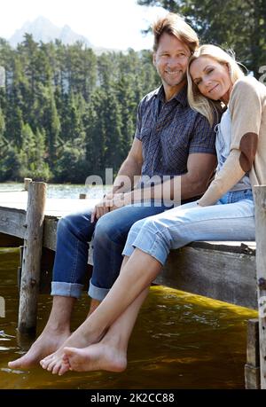 Always comfortable in eachothers company. Shot of a loving mature couple sitting on a pier out on a lake in the countryside. Stock Photo
