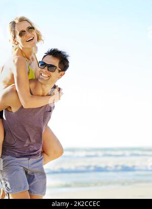 Strong enough for both of us. Shot of a man carrying his girlfriend on the beach. Stock Photo