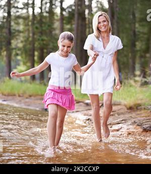 Lets go this way mom. A cute little girl running through a wilderness stream with her mother. Stock Photo