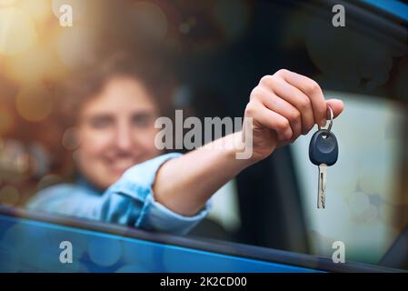 Whos up for a drive. Shot of a happy young woman holding the keys to a new car. Stock Photo