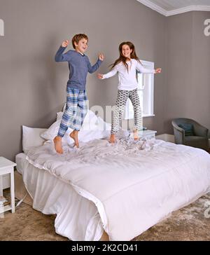 What mom and dad dont know wont hurt them. Shot of a brother and sister jumping on their parents bed. Stock Photo