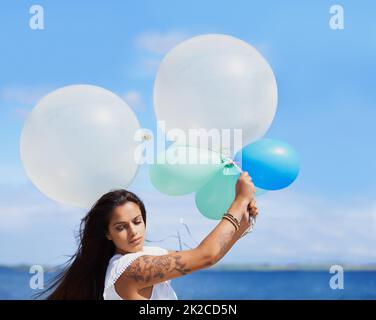 Sometimes you have to hold on tightly. Cropped shot of a gorgeous tattooed young woman holding balloons. Stock Photo