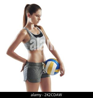 Thinking about the game. Cropped shot of a young female athlete holding a volleyball against a white background. Stock Photo